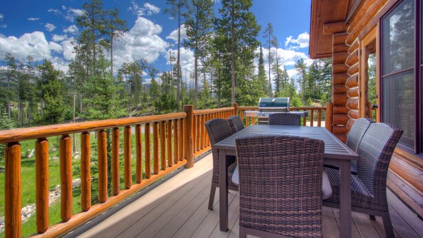 A wooden deck with wicker furniture, a grill, and a view of a forest. - Red Cloud 4 | Ski-in/Out Cabin, Hot Tub, Sleeps 12 (Big Sky)