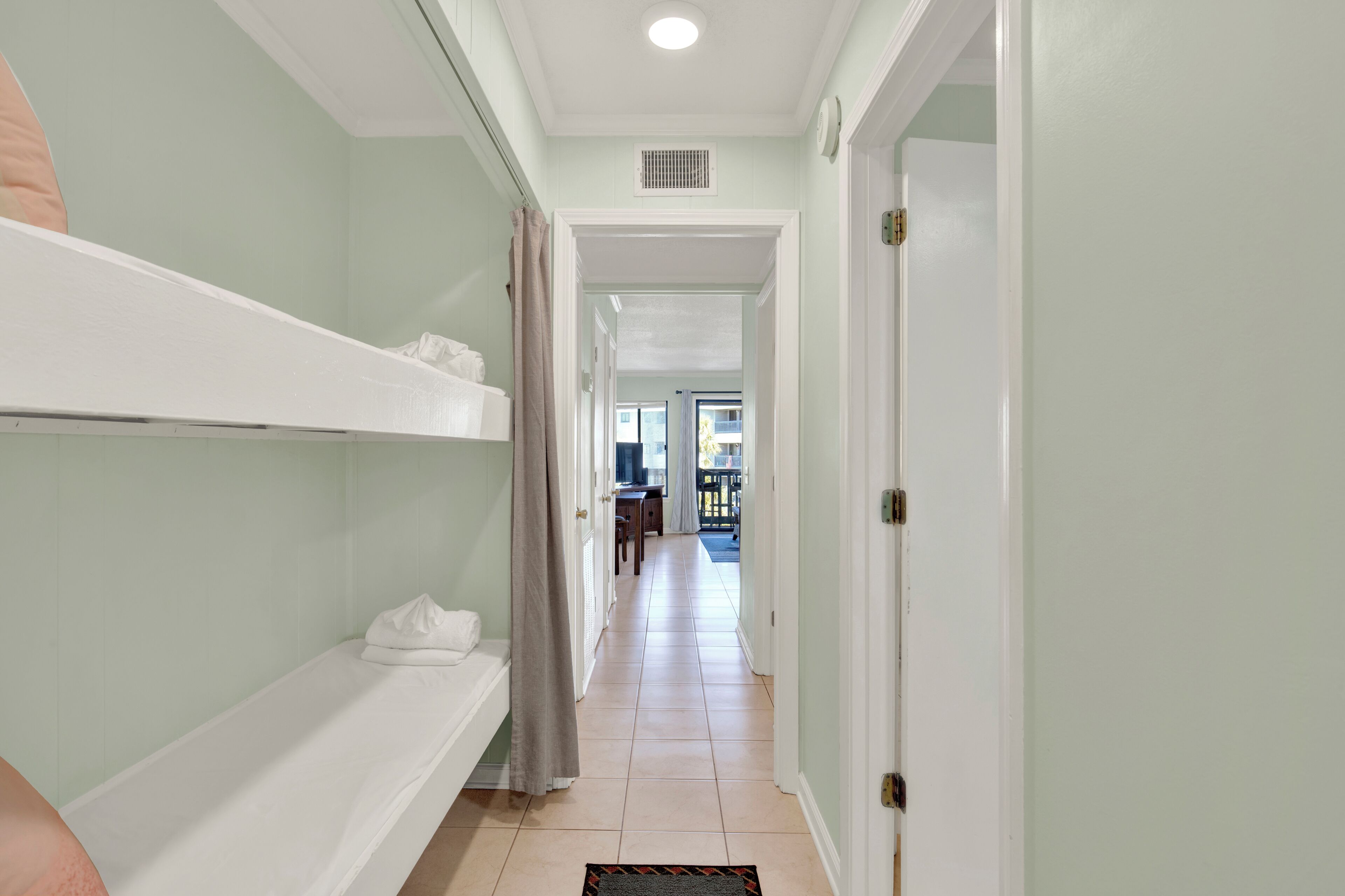 A hallway with a bunk bed, a door, and a view into another room.