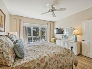 A bedroom with a bed, a dresser, a mirror, a ceiling fan, and a window with curtains.