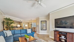 A living room with a blue sofa, a coffee table, a TV stand, and a ceiling fan.