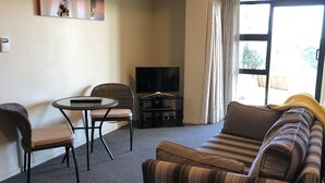 Een woonkamer met een bank, stoelen, een bijzettafeltje, een televisie en een raam met gordijnen.