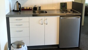 Een kleine keuken met een magnetron, fornuis, spoelbak en een kleine koelkast.