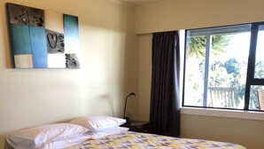 Een netjes opgemaakt bed met een bedsprei met dessin, een bedlamp, een nachtkastje en een raam met gordijnen.