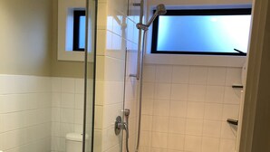 Een moderne badkamer met een douchecabine van glas, een toilet en een klein raam boven de douche.