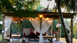 An outdoor patio with wooden tables and chairs, draped white fabric, and string lights. - STAY LOVE PLAY at Fusion Beach Villas GARDEN studio, 1/2 mi west of Jobos Beach (Bo. Bajuras, Jobos, Isabela)