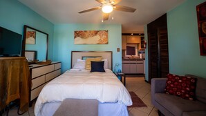 A bedroom with a bed, a desk, a chair, a ceiling fan, and a kitchenette in the background. - STAY LOVE PLAY at Fusion Beach Villas GARDEN studio, 1/2 mi west of Jobos Beach (Bo. Bajuras, Jobos, Isabela)