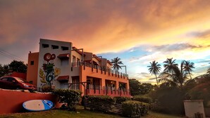 A building with a balcony, a red car parked in front, and a surfboard on the ground. - STAY LOVE PLAY at Fusion Beach Villas GARDEN studio, 1/2 mi west of Jobos Beach (Bo. Bajuras, Jobos, Isabela)