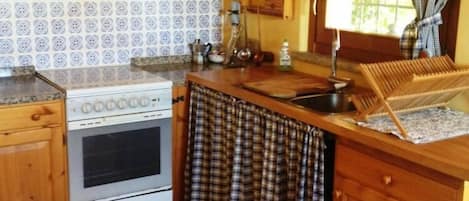A kitchen with wooden cabinets, a tiled backsplash, a stove, and a window with curtains.
