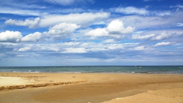 Une plage avec un ciel dégagé et quelques nuages.