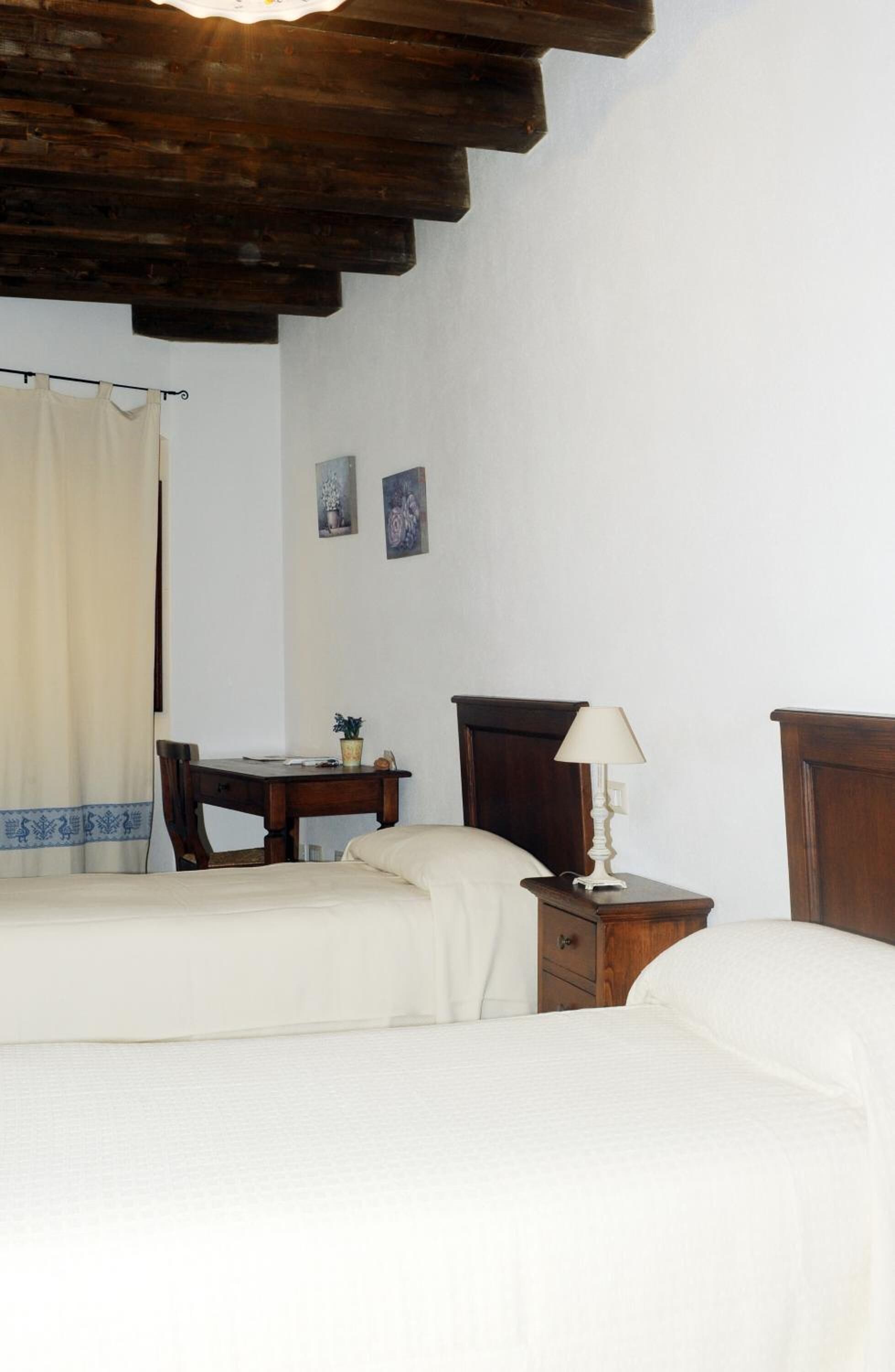 A bedroom with a wooden ceiling, a bed, a bedside table with a lamp, a desk, and a chair.