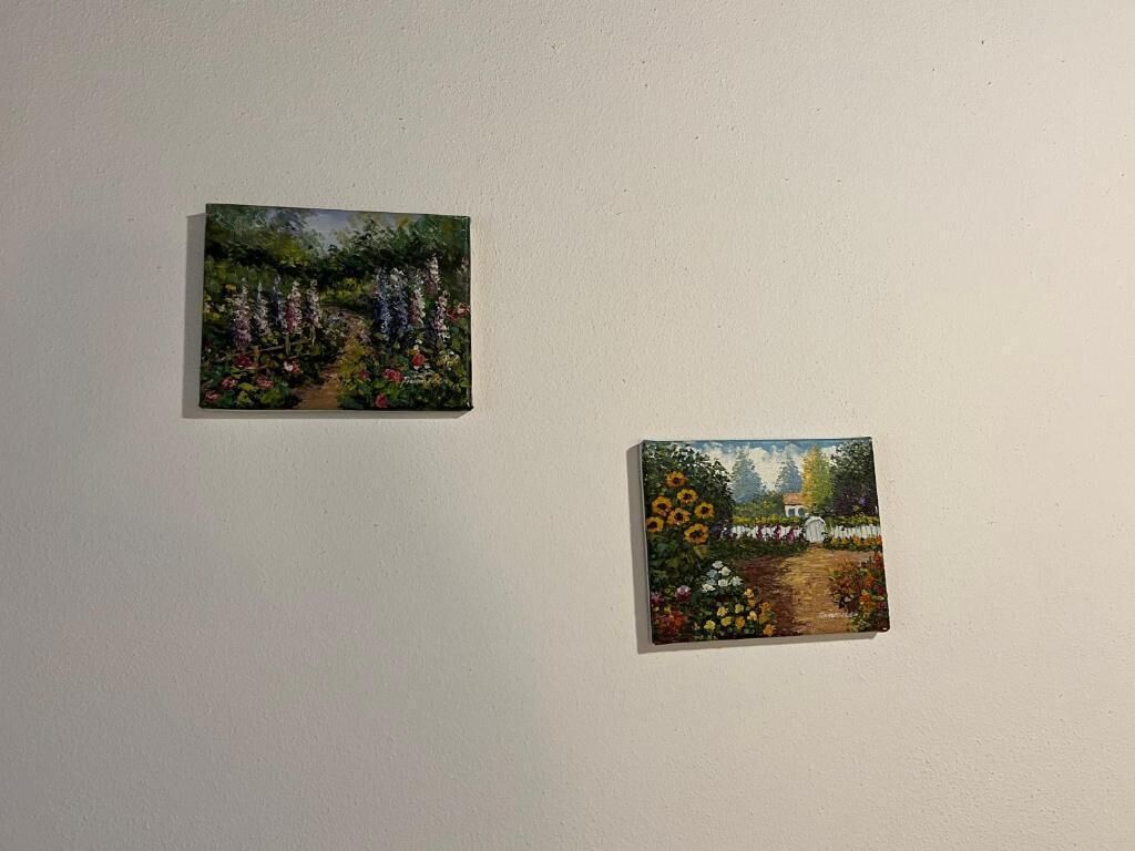 Two small paintings of gardens on a plain wall.