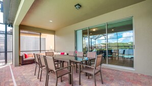 An outdoor patio with a brick floor, a dining table with chairs, and a seating area with a sofa and cushions. - Windsor at Westside Exec Villas- 1639la (Kissimmee)