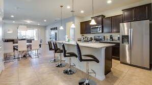 Une cuisine moderne avec des meubles de couleur sombre, des appareils en acier inoxydable et un îlot central doté de tabourets de bar.