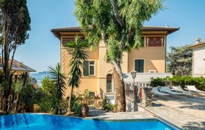 A Mediterranean-style building with a pool, surrounded by lush greenery and a clear view of the sea. - Nice apartment in Rapallo with outdoor swimming pool (Rapallo)