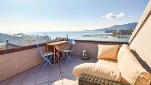 Un balcon avec un canapé en osier, une table en bois et des chaises pliantes bleues.