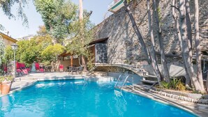 Une piscine bordée de chaises longues rouges, un mur en pierre et une terrasse en bois.