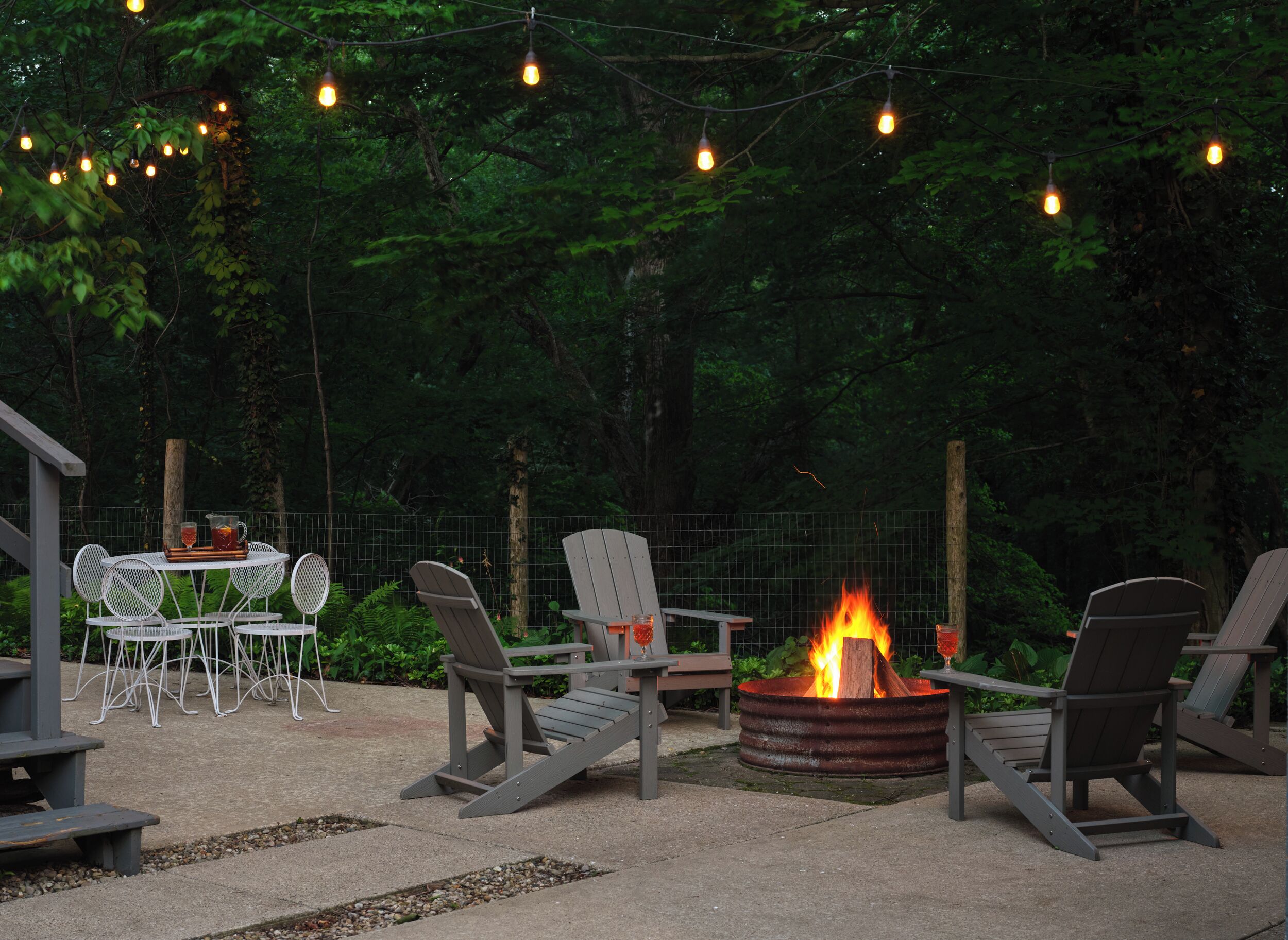 An outdoor seating area with Adirondack chairs, a fire pit, and string lights.