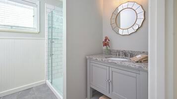 A bathroom with a glass shower enclosure, a vanity with a marble countertop, and a wall-mounted mirror.