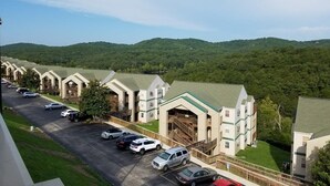 Un hôtel composé de plusieurs bâtiments à étages, doté d’un parking et offrant une vue sur des collines verdoyantes en arrière-plan.