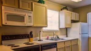 Une cuisine de taille réduite avec des meubles blancs, un four à micro-ondes, une cuisinière, un évier et un lave-vaisselle.