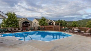 Une piscine entourée de bâtiments et d’arbres, avec des chaises longues et une terrasse en bois.