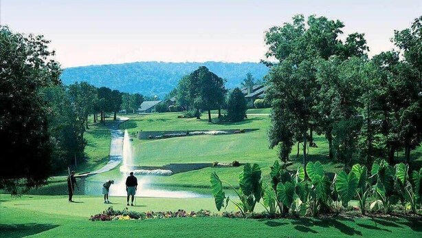 Un parcours de golf agrémenté d’un plan d’eau, d’arbres et offrant une vue sur une chaîne de montagnes lointaine.