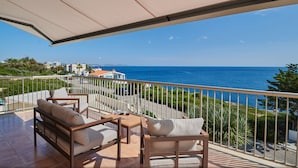 Ein Balkon mit Meerblick, möbliert mit einer Couch, Stühlen und einem Tisch mit einem Glas.