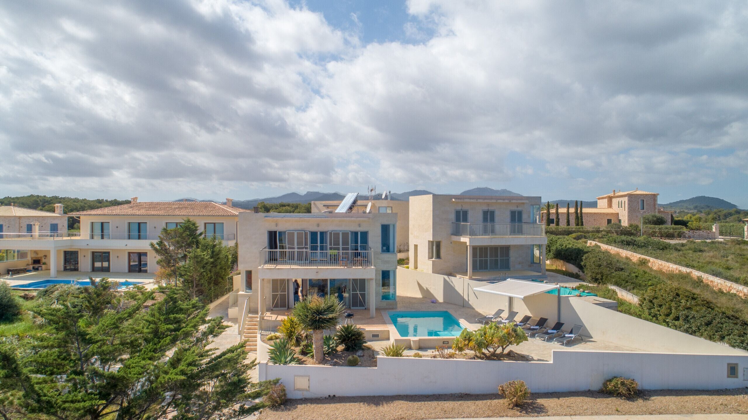 A modern villa with a swimming pool, multiple balconies, and a view of the surrounding landscape.
