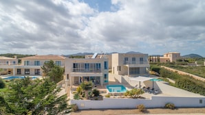Eine moderne Villa mit Swimmingpool, mehreren Balkonen und Blick auf die umliegende Landschaft.