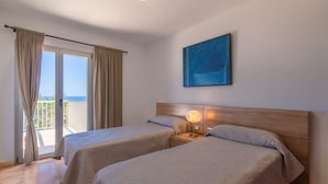 Ein Hotelzimmer mit zwei Betten, einem hölzernen Kopfteil, einem Nachttisch mit Lampe und einem großen Fenster mit Vorhängen.