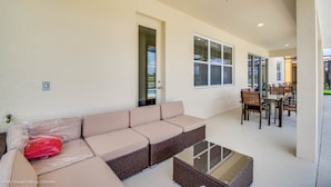 Ein überdachter Patio-Bereich mit einem beigefarbenen Ecksofa, einem Couchtisch mit Glasplatte und einem Esstisch.