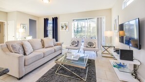 A modern living room with a sofa, armchairs, a glass coffee table, a TV, and a laptop on a white console. - Solterra Exec Villas- 4201oview (Davenport)