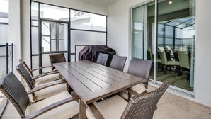 Ein Essbereich mit Holztisch und Korbstühlen, großen Fenstern und einer Glastür zum Balkon.