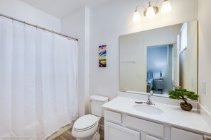 A bathroom with a white toilet, a white sink, a large mirror, and a shower curtain. - Solterra Exec Villas- 6104boa (Davenport)