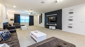 A modern living room with a flat-screen TV, ceiling fans, and a large window with curtains.