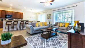 A spacious living room with a sofa, coffee table, and a dining area with bar stools.