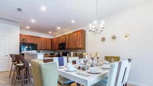 A modern kitchen with wooden cabinets, a dining area with a white table set for four, and a chandelier.
