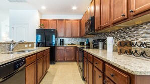 A modern kitchen with wooden cabinets, granite countertops, stainless steel appliances, and a tiled backsplash.