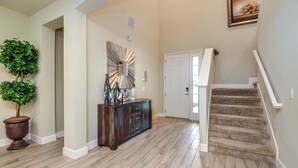 Un hall d’entrée spacieux avec un escalier en bois, une plante en pot, une console en bois foncé et un miroir décoratif.