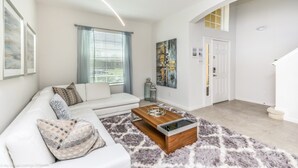 A modern living room with a white sofa, a wooden coffee table, and a fluffy rug. There is a door with a glass panel and a painting on the wall.