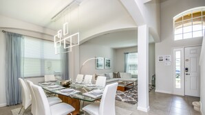 A modern dining area with a glass table, white chairs, and a sofa in the background.