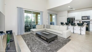 A modern living room with a sectional sofa, a coffee table, and a kitchen area with white cabinets and black bar stools.