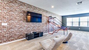 Ein modernes Wohnzimmer mit Backsteinwand, einer an der Wand befestigten Fernseher, einem Basketballkorb und einem gepolsterten Sessel.