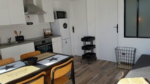 Kompakti keittiö, jossa on valkoiset kaapit, mikroaaltouuni ja liesi. Keittiössä on ruokapöytä tuoleineen sekä musta tarjoiluvaunu.