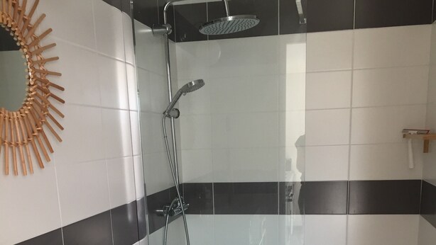 A modern bathroom with a white sink, wooden vanity, a toilet, a shower with a handheld showerhead, and a sunburst mirror on the wall. - VACATION HOME, EVERYTHING BY BIKE! (NOIRMOUTIER)