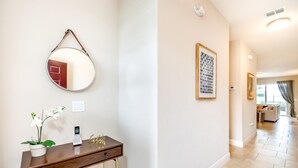 Un couloir avec un grand miroir rond, une petite table sur laquelle se trouvent un téléphone et une plante, et une œuvre d’art encadrée accrochée au mur.