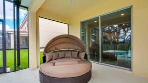 Un espacio de estar al aire libre con techo, una puerta corredera de vidrio y vista a una piscina.