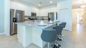 Una cocina moderna con armarios blancos, electrodomésticos de acero inoxidable, encimera de granito y taburetes de bar.