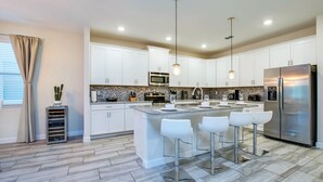 A modern kitchen with white cabinets, stainless steel appliances, and a central island with bar stools. - Solterra Exec Villas- 5416sc (Davenport)