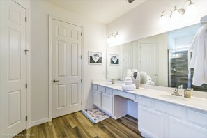 Un baño con muebles blancos, un espejo grande y suelo de madera.